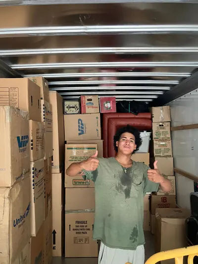 A mover giving two thumbs up in front of a wall of stacked moving boxes