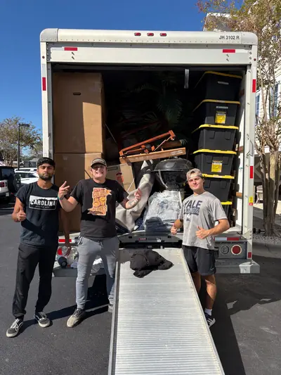 Three crew members standing at the ramp of a packed moving truck