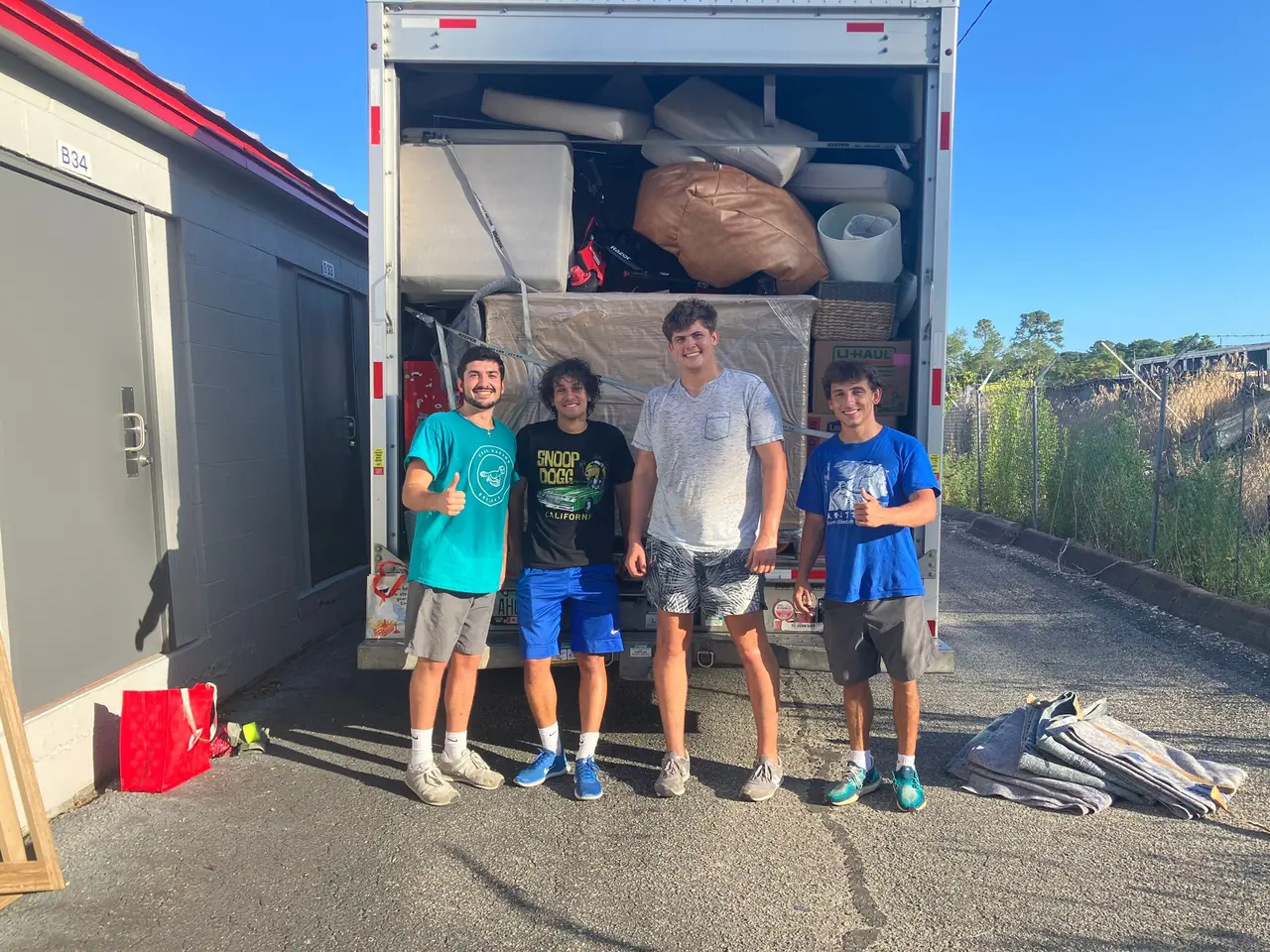 Four Express Movers crew members in front of a fully loaded truck beside a row of storage units