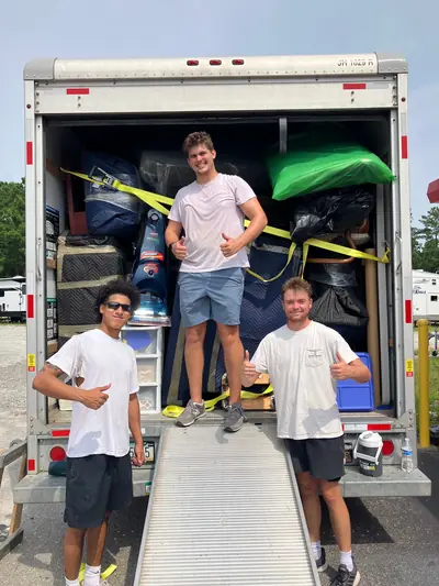 Three crew members at the back of a truck with the load strapped down