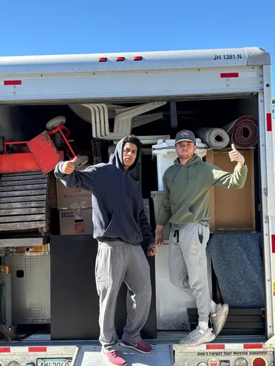 Two crew members giving a thumbs up at the back of a loaded truck