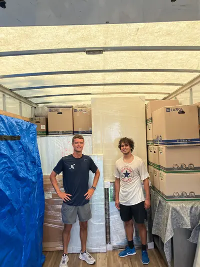 Two movers inside a packed truck with wrapped furniture
