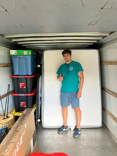 A mover giving a thumbs up next to a mattress and totes loaded in a truck