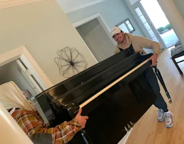 Two movers carrying an upright piano through a house