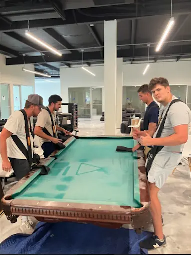 Four crew members lifting a pool table with moving straps