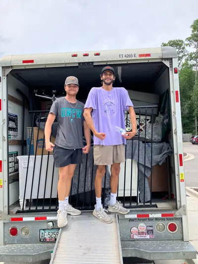 Two movers on a truck ramp, one wearing a UNCW shirt