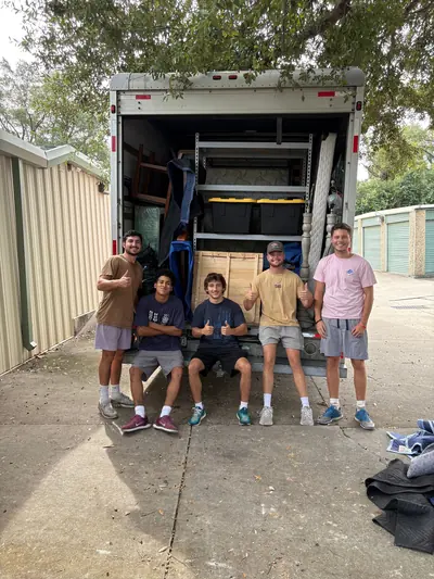 Five crew members on the tailgate of a loaded moving truck