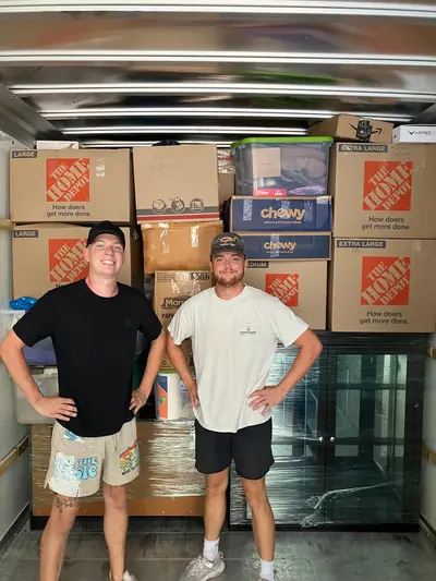 Two movers standing in front of boxes stacked floor to ceiling in a truck